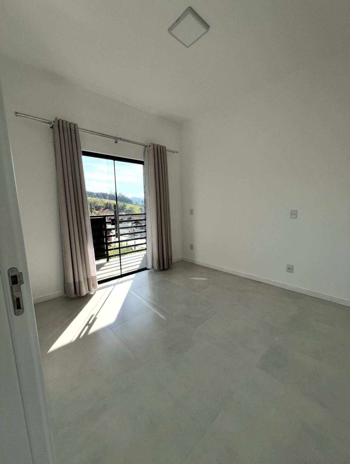 Dormitório com porta de vidro para a sacada e cortinas